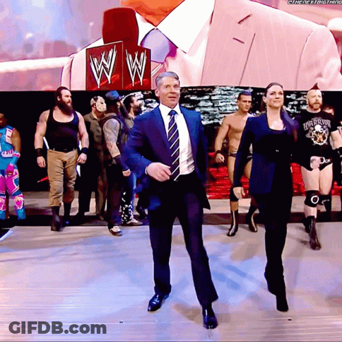 A Man In A Suit And Tie Is Dancing In Front Of A Sign That Says Wwe GIF