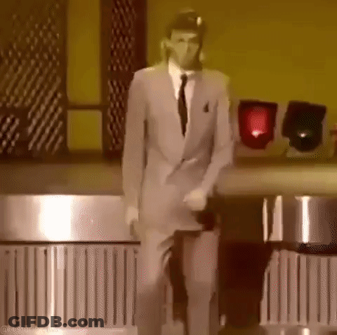 A Man In A Suit And Tie Is Dancing On A Stage In A Dark Room . GIF