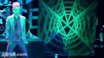 A Man In A Suit And Tie Is Dancing On A Stage In Front Of A Green Spider Web GIF