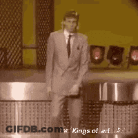A Man In A Suit And Tie Is Dancing On A Stage In Front Of A Microphone . GIF