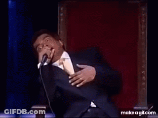A Man In A Suit And Tie Is Dancing On A Stage In Front Of A Microphone . GIF