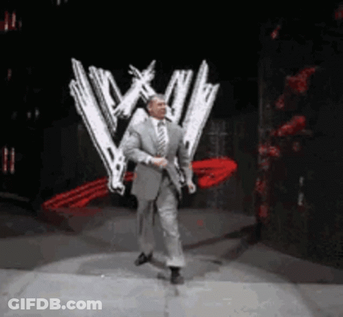 A Man In A Suit And Tie Is Dancing On A Stage In Front Of A Wwe Logo . GIF