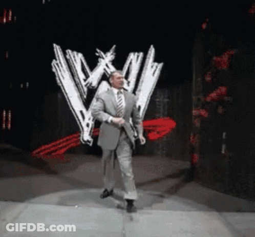 A Man In A Suit And Tie Is Dancing On A Stage In Front Of A Wwe Logo GIF