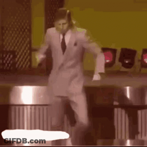 A Man In A Suit And Tie Is Dancing On A Stage In Front Of A Yellow Wall . GIF