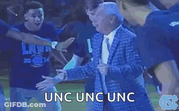 A Man In A Suit And Tie Is Dancing With A Group Of People In A Circle . GIF