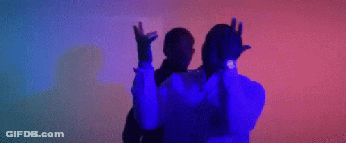 A Man In A Suit And Tie Is Dancing With His Arms In The Air In A Dark Room . GIF