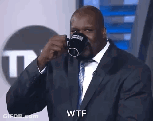 A Man In A Suit And Tie Is Drinking From A Coffee Mug And Says Wtf GIF