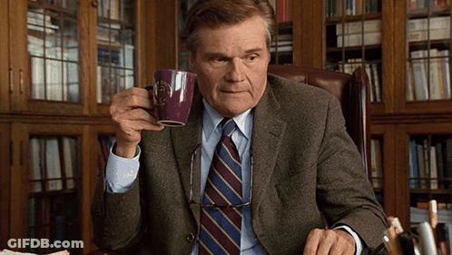 A Man In A Suit And Tie Is Drinking From A Mug That Says ' Boston ' On It GIF