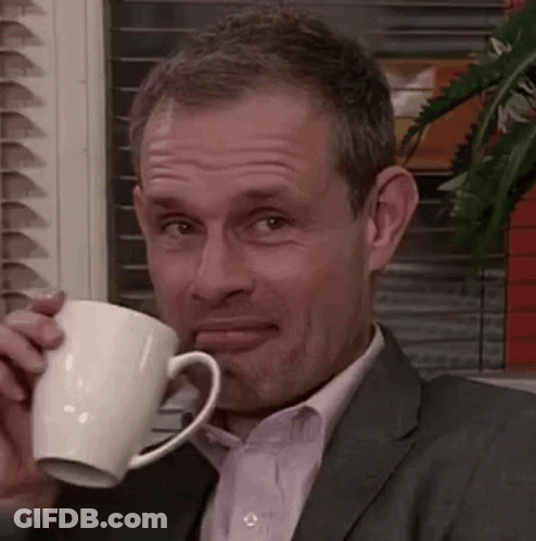 A Man In A Suit And Tie Is Drinking From A White Mug . GIF