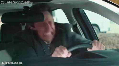 A Man In A Suit And Tie Is Driving A Car With A Caption That Says Latenightseth GIF