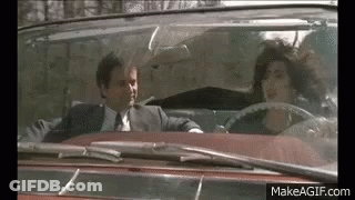 A Man In A Suit And Tie Is Driving A Convertible With A Woman In The Back Seat . GIF