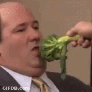 A Man In A Suit And Tie Is Eating Broccoli From A Person 'S Hand . GIF