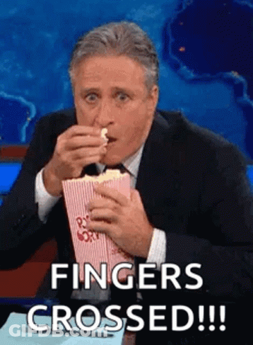 A Man In A Suit And Tie Is Eating Popcorn And Saying `` Fingers Crossed ! '' GIF