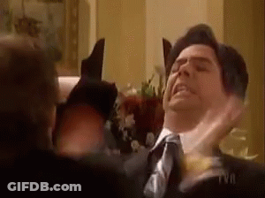 A Man In A Suit And Tie Is Getting Punched In The Face By Another Man . GIF