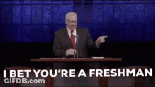 A Man In A Suit And Tie Is Giving A Speech In Front Of A Microphone And Pointing At The Audience . GIF