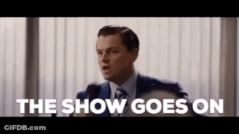 A Man In A Suit And Tie Is Giving A Speech In Front Of A Microphone And Saying The Show Goes On . GIF