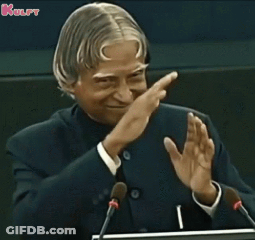 A Man In A Suit And Tie Is Giving A Speech In Front Of Microphones And Applauding . GIF