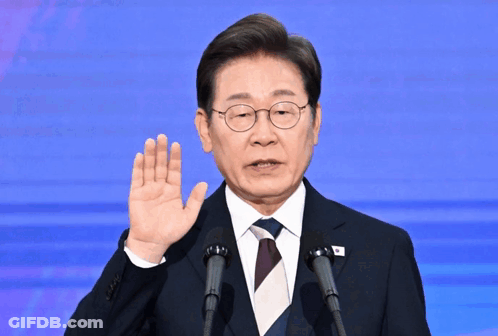 A Man In A Suit And Tie Is Giving A Speech In Front Of Two Microphones GIF
