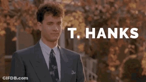 A Man In A Suit And Tie Is Giving A Thumbs Up In Front Of A Sign That Says T. Hanks . GIF