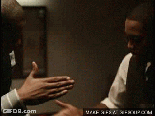 A Man In A Suit And Tie Is Giving Another Man A High Five GIF