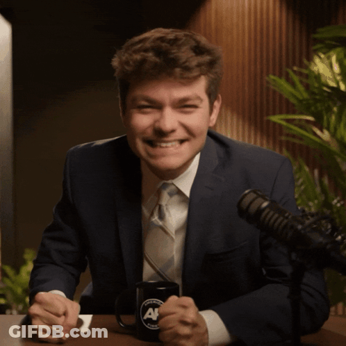 A Man In A Suit And Tie Is Giving The Middle Finger In Front Of A Microphone GIF