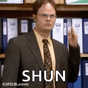 A Man In A Suit And Tie Is Giving The Middle Finger In Front Of A Shelf Of Folders . GIF