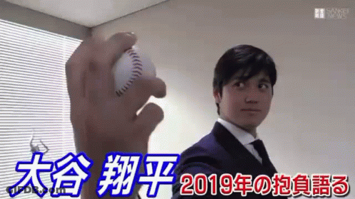 A Man In A Suit And Tie Is Holding A Baseball In His Right Hand . GIF