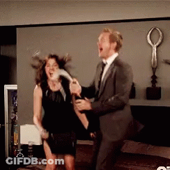 A Man In A Suit And Tie Is Holding A Bottle Of Champagne And A Woman In A Black Dress Is Holding A Feather GIF