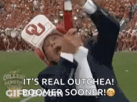 A Man In A Suit And Tie Is Holding A Bottle Of Ketchup While Wearing A Helmet And A Hat . GIF
