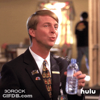 A Man In A Suit And Tie Is Holding A Bottle Of Water With The Hulu Logo In The Background GIF