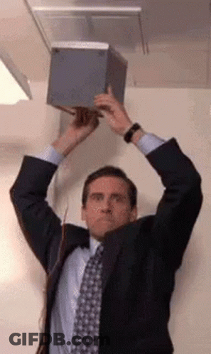 A Man In A Suit And Tie Is Holding A Box In His Hands . GIF