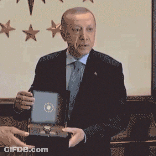 A Man In A Suit And Tie Is Holding A Box GIF