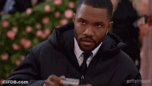 A Man In A Suit And Tie Is Holding A Camera And Looking At It . GIF