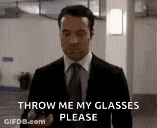 A Man In A Suit And Tie Is Holding A Cell Phone And Asking To Throw Me My Glasses Please . GIF