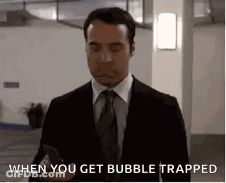 A Man In A Suit And Tie Is Holding A Cell Phone And Saying `` When You Get Bubble Trapped '' . GIF
