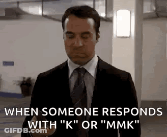A Man In A Suit And Tie Is Holding A Cell Phone In A Parking Garage . GIF