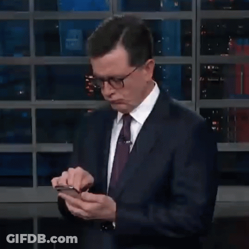 A Man In A Suit And Tie Is Holding A Cell Phone In His Hands GIF