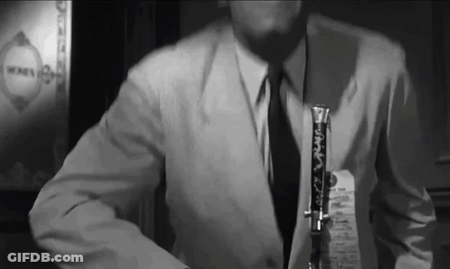 A Man In A Suit And Tie Is Holding A Clarinet GIF