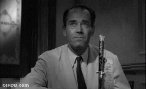 A Man In A Suit And Tie Is Holding A Clarinet In His Right Hand . GIF