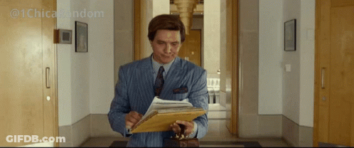A Man In A Suit And Tie Is Holding A Clipboard And Looking At It GIF