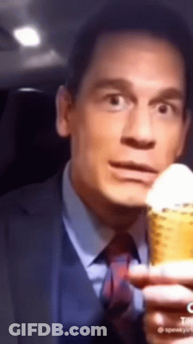 A Man In A Suit And Tie Is Holding A Corn On The Cob And Making A Funny Face . GIF