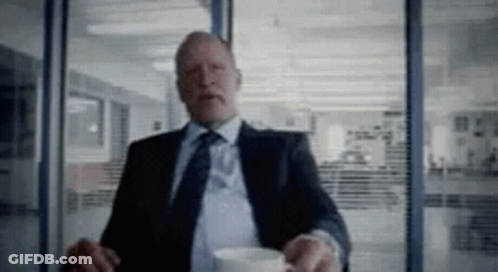 A Man In A Suit And Tie Is Holding A Cup Of Coffee . GIF