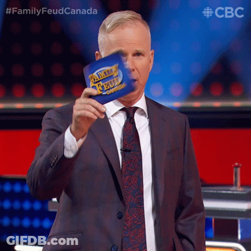 A Man In A Suit And Tie Is Holding A Family Feud Card In Front Of His Face GIF