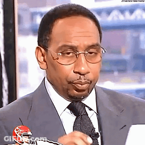 A Man In A Suit And Tie Is Holding A Football Helmet And Making A Funny Face . GIF