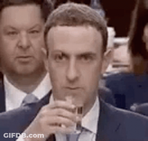 A Man In A Suit And Tie Is Holding A Glass Of Wine In Front Of A Crowd Of People . GIF