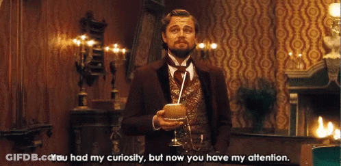 A Man In A Suit And Tie Is Holding A Glass With A Straw And Says You Had My Curiosity But Now You Have My Attention GIF