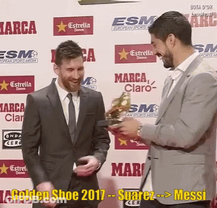 A Man In A Suit And Tie Is Holding A Golden Shoe While Another Man Looks On GIF
