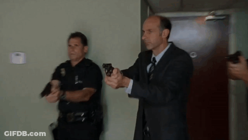 A Man In A Suit And Tie Is Holding A Gun GIF