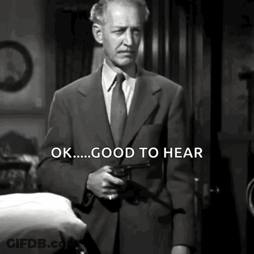 A Man In A Suit And Tie Is Holding A Gun And Says " Ok Good To Hear " GIF