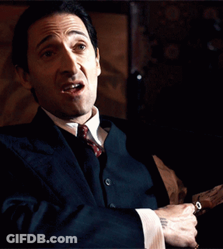 A Man In A Suit And Tie Is Holding A Gun In His Hand GIF